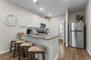 A modern kitchen with a central island, bar stools, stainless steel appliances, and a wall clock. - Quiet Haven Amidst the Action! No Steps! - 3 Bed 2 Bath Condo (Branson)