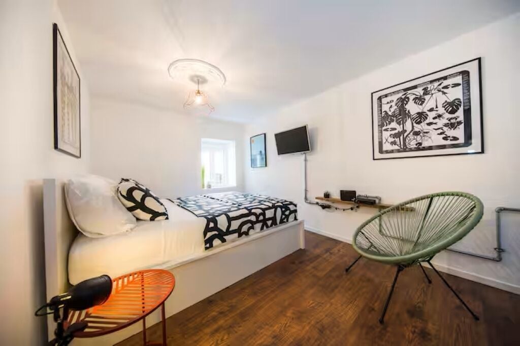A bedroom with a bed, a chair, a TV, and artwork on the walls.