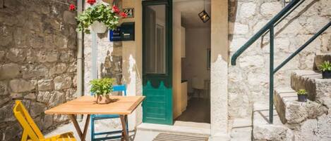 A stone building with a green door, a wooden table with chairs, and a staircase.