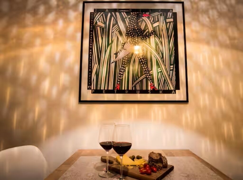 A framed artwork on a wall, a table with two glasses of red wine, and a variety of food items.