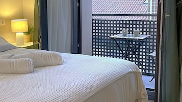 A bedroom with a bed, a nightstand, a lamp, and a view of a balcony with a table and chairs.