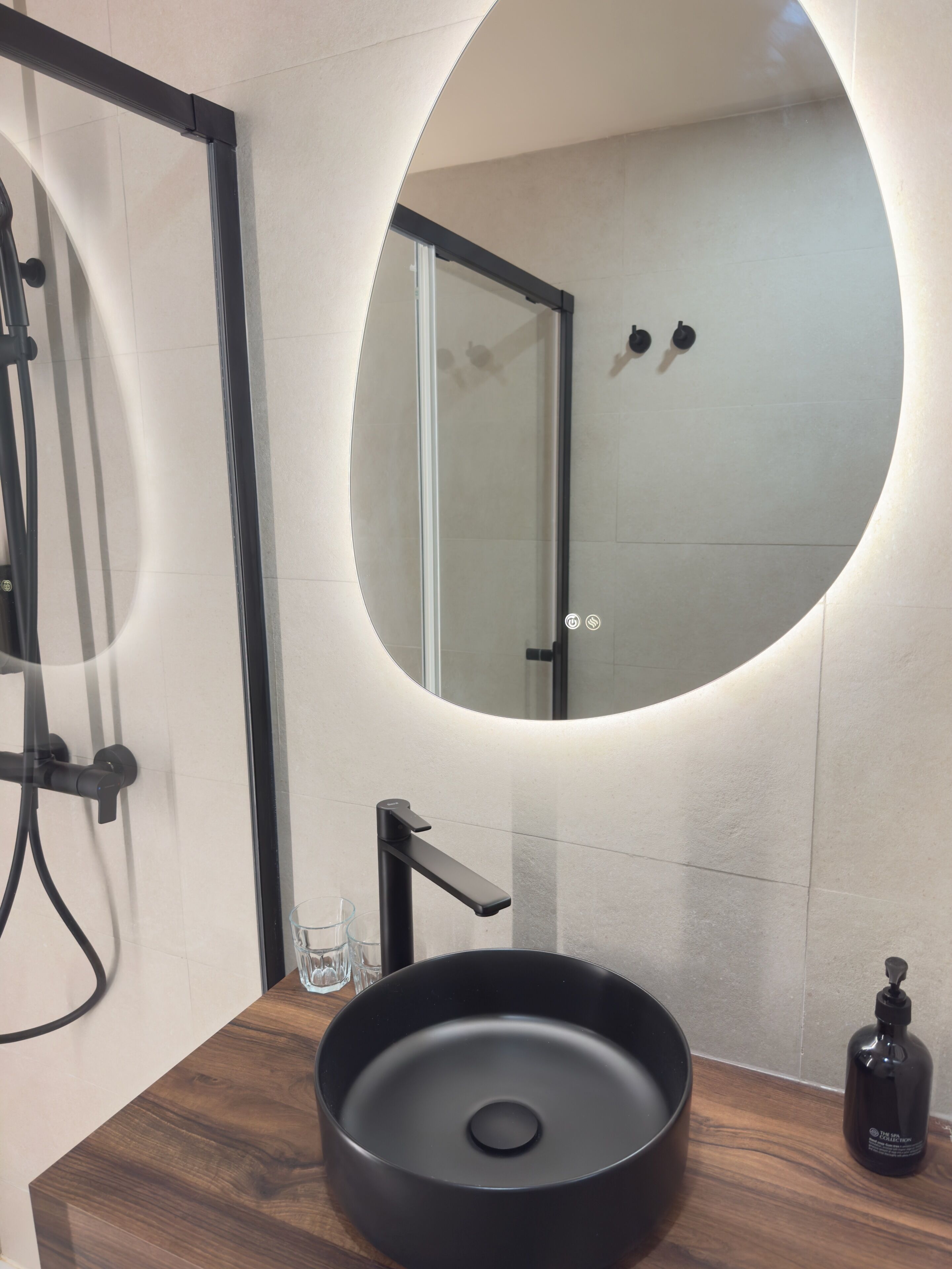 A modern bathroom with a round mirror, a black sink, and a handheld showerhead.