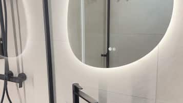 A modern bathroom with a round mirror, a black sink, and a handheld showerhead.