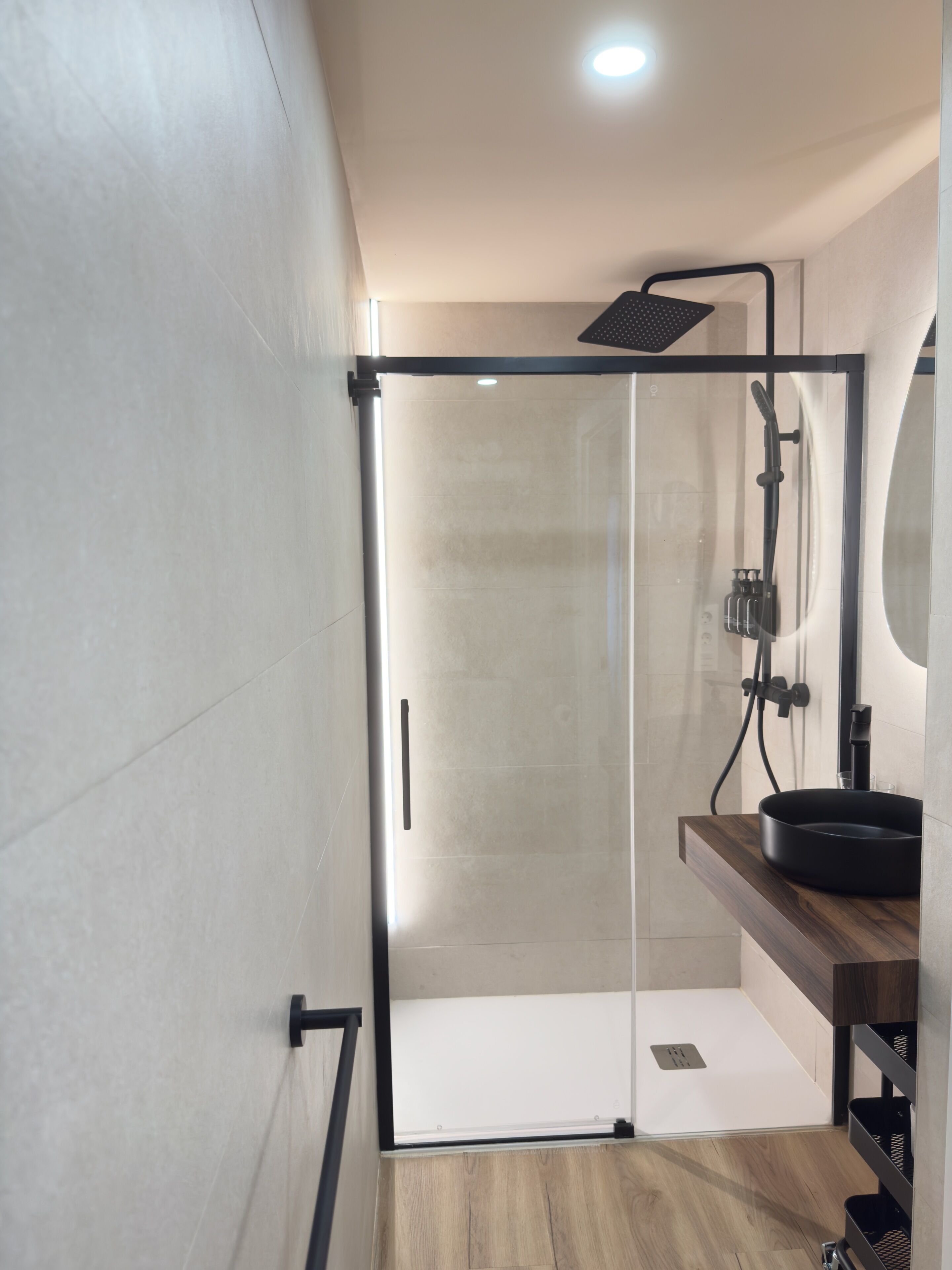 Un baño moderno con cabina de ducha de vidrio, tocador de madera y un espejo.