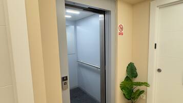 Ascensor con barandilla, señal de no fumar y una planta en maceta al lado de una puerta.