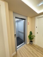 Ascensor con barandilla, señal de no fumar y una planta en maceta al lado de una puerta.