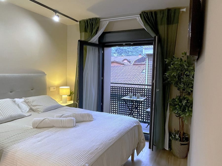 A hotel room with a bed, a nightstand, a lamp, a potted plant, and a view of a balcony.