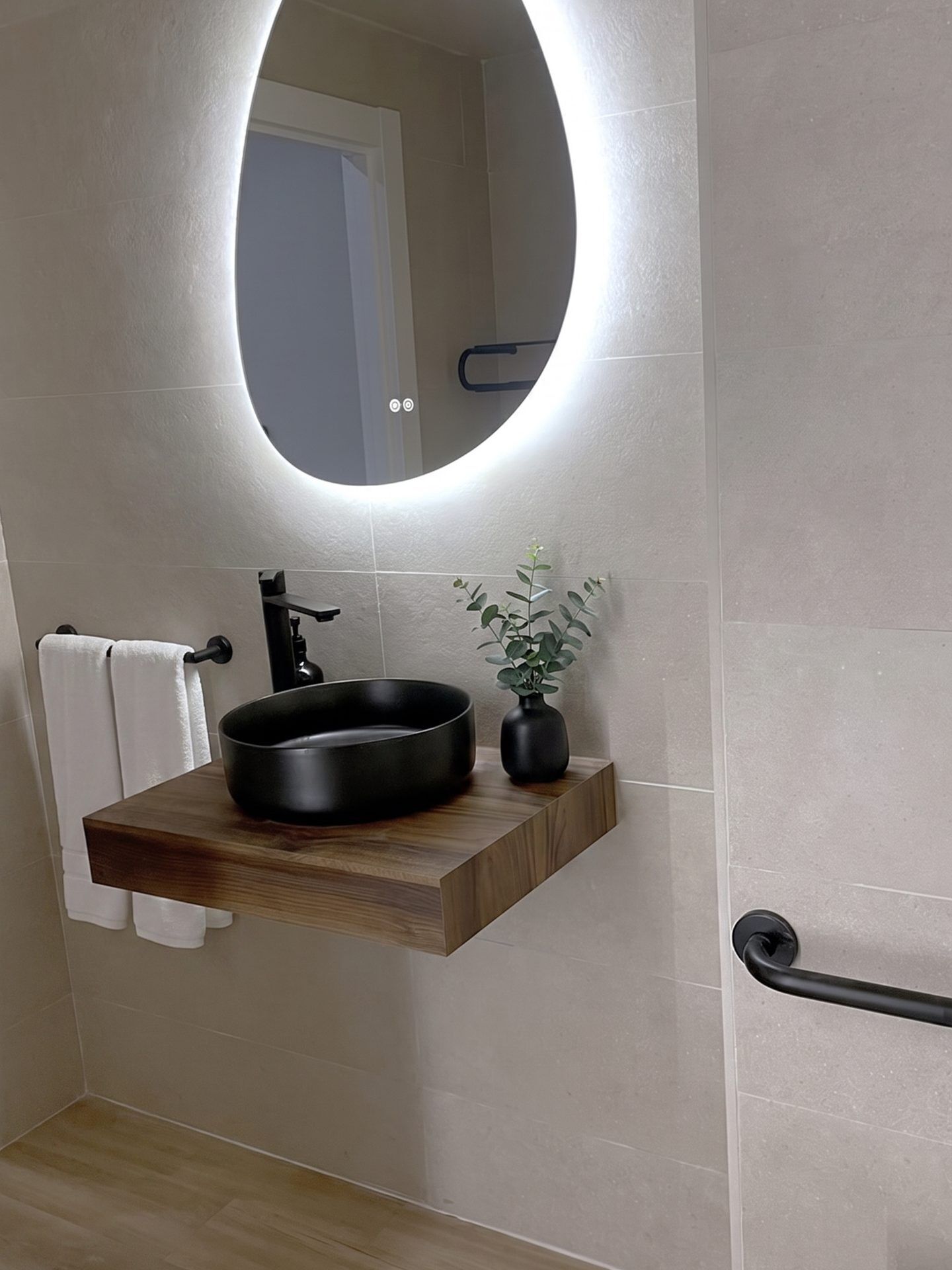 A bathroom with a round mirror, a black sink, a towel rack, and a potted plant.