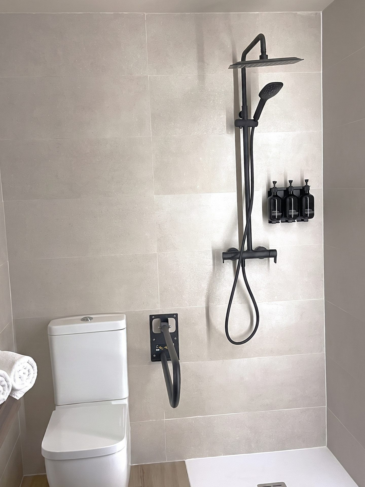 A modern bathroom with a toilet, a shower unit, and a wall-mounted soap dispenser.