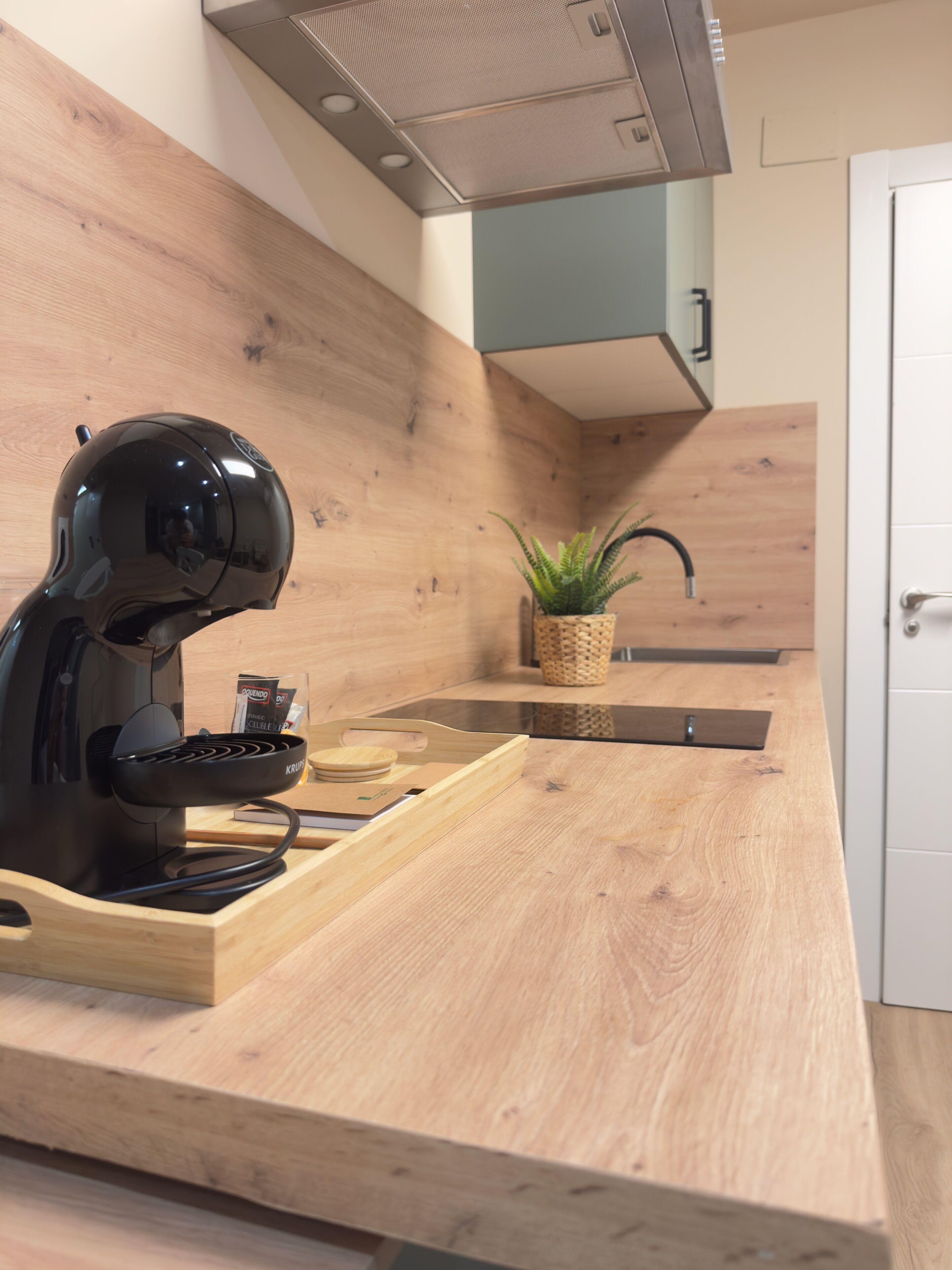 A modern kitchen with a built-in coffee machine, wooden countertop, and a small potted plant.