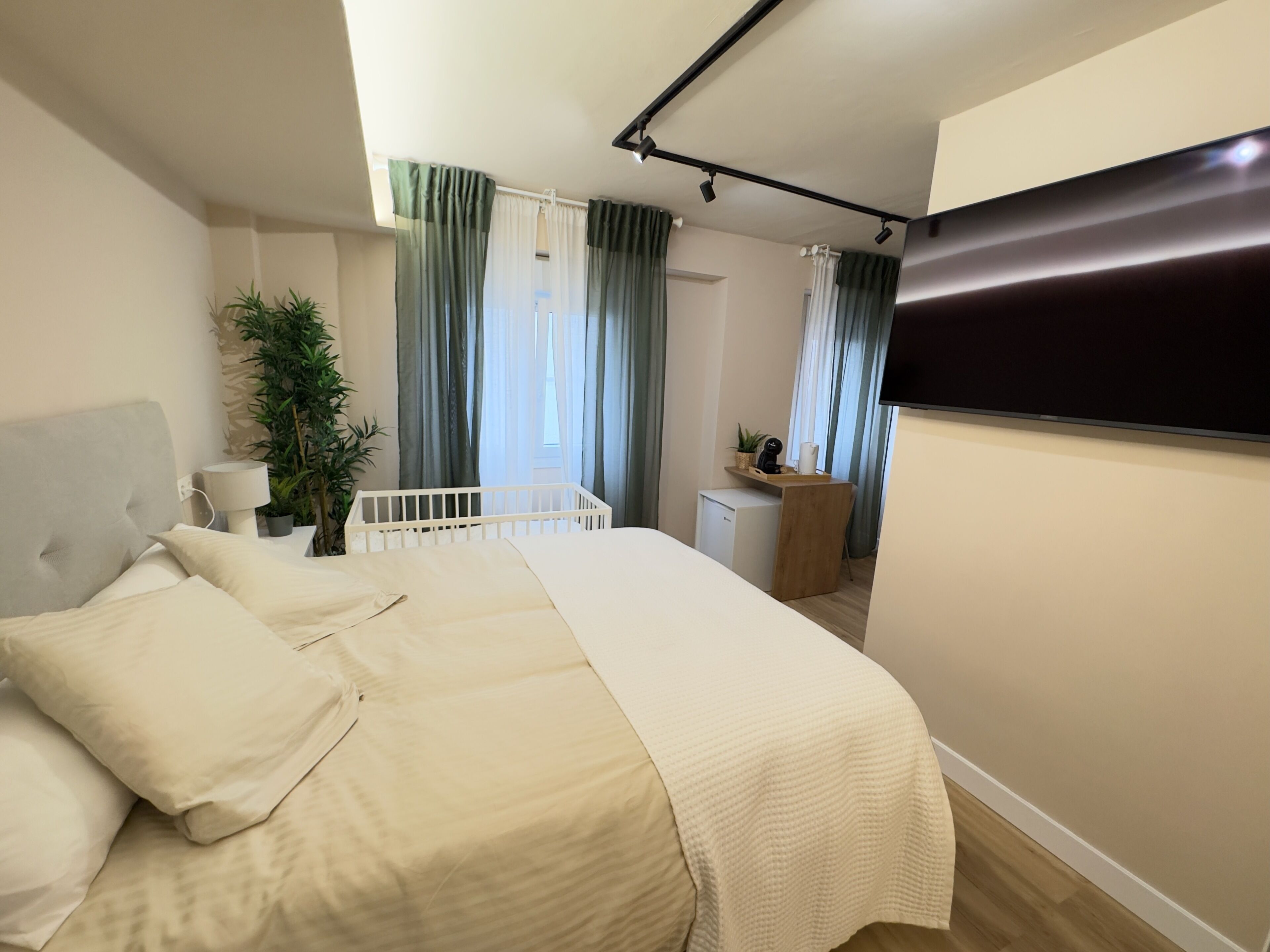 Un dormitorio con cama, mesita de noche, lámpara, planta en maceta y un pequeño escritorio con silla.