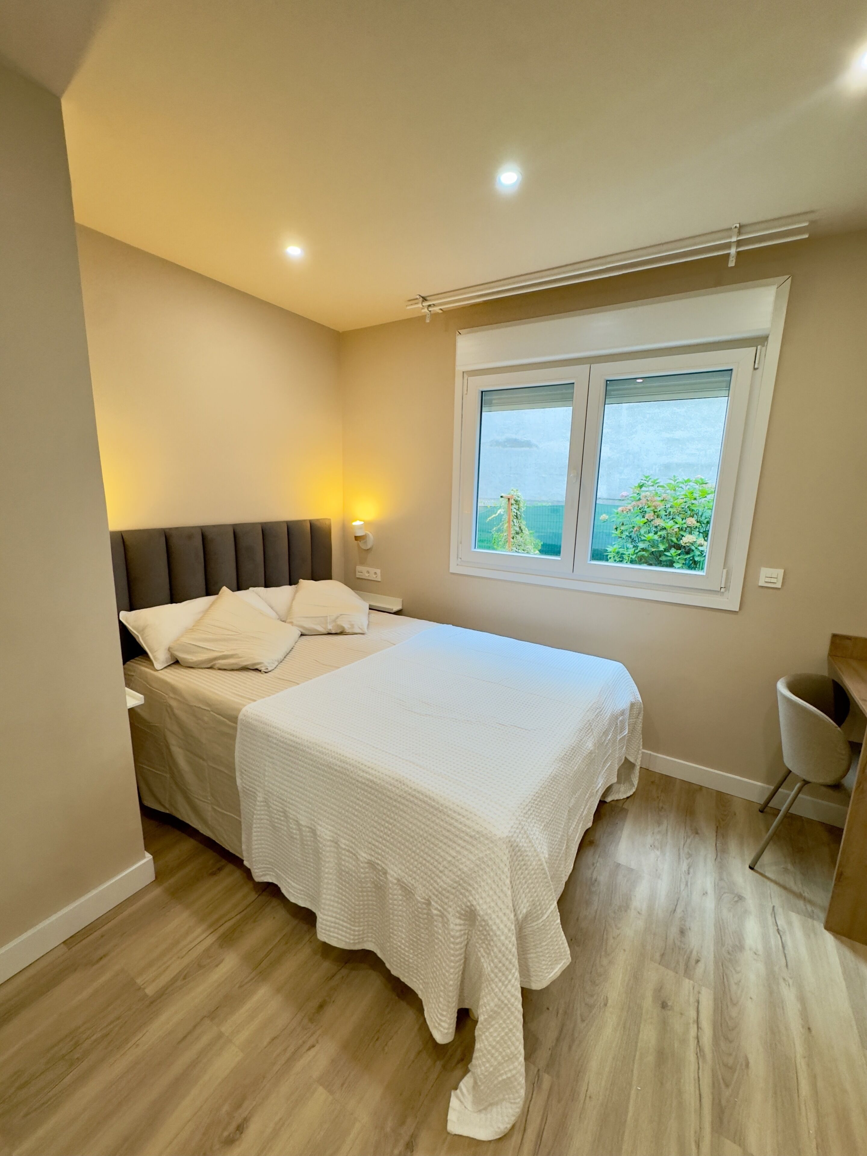 Een slaapkamer met een bed, nachtkastje en een raam met uitzicht.