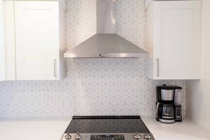 Uma cozinha com exaustor de aço inoxidável, cafeteira e painel de backsplash com padrão hexagonal.