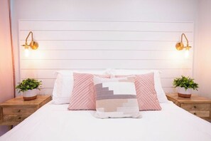 Ein ordentlich bezogenes Bett mit gemusterten Kissen, zwei Nachttische mit Topfpflanzen und Wandleuchten.