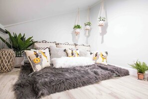 Ein Schlafzimmer mit einem Bett, Kissen, einem flauschigen Teppich, hängenden Pflanzen und einer Topfpflanze.