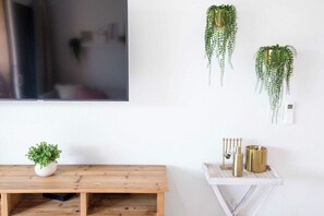 Um quarto com uma mesa de madeira, uma planta em vaso, uma planta pendente e uma pequena mesa branca com objetos decorativos.