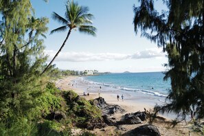 Uma praia com pessoas, palmeiras e edifícios ao fundo.