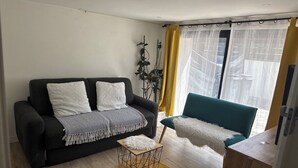 Una sala de estar con un sofá negro, un sillón verde azulado, una mesita de madera y una alfombra amarilla.