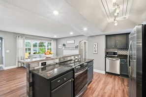 A modern kitchen with a central island, stainless steel appliances, and a view to the outdoors. - Heated Pool + Spa, Fenced Yard, Fire Pit, Sleeps 8, 15 Min to AMI (Bradenton)