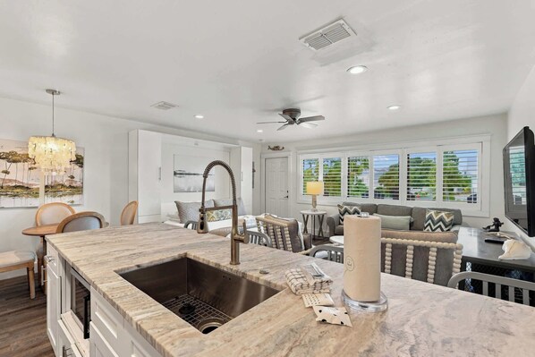 A modern kitchen with a built-in sink, a dining area with a table and chairs, and a seating area with a sofa and a TV. - Suite Y'all | 2-Min Walk to Beach | Pet Friendly (Santa Rosa Beach)
