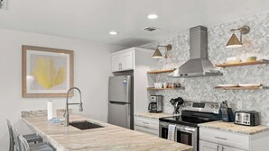 A modern kitchen with a marble countertop, stainless steel appliances, and pendant lighting. - Suite Y'all | 2-Min Walk to Beach | Pet Friendly (Santa Rosa Beach)