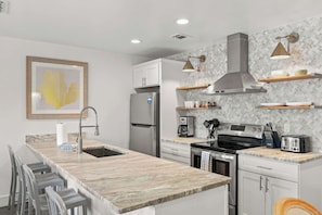A modern kitchen with a marble countertop, stainless steel appliances, and pendant lighting. - Suite Y'all | 2-Min Walk to Beach | Pet Friendly (Santa Rosa Beach)
