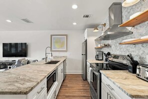 A modern kitchen with a central island, built-in appliances, and a dining area with a flat-screen TV. - Suite Y'all | 2-Min Walk to Beach | Pet Friendly (Santa Rosa Beach)