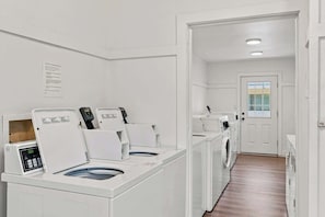 A laundry room with multiple washing machines and dryers, a wooden floor, and a white door with a window. - Suite Y'all | 2-Min Walk to Beach | Pet Friendly (Santa Rosa Beach)