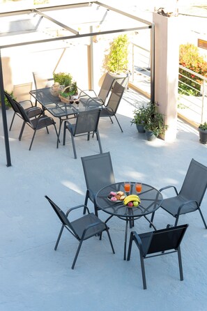 Un'area patio esterna con tavoli e sedie in metallo, piante in vaso e vista sui dintorni.
