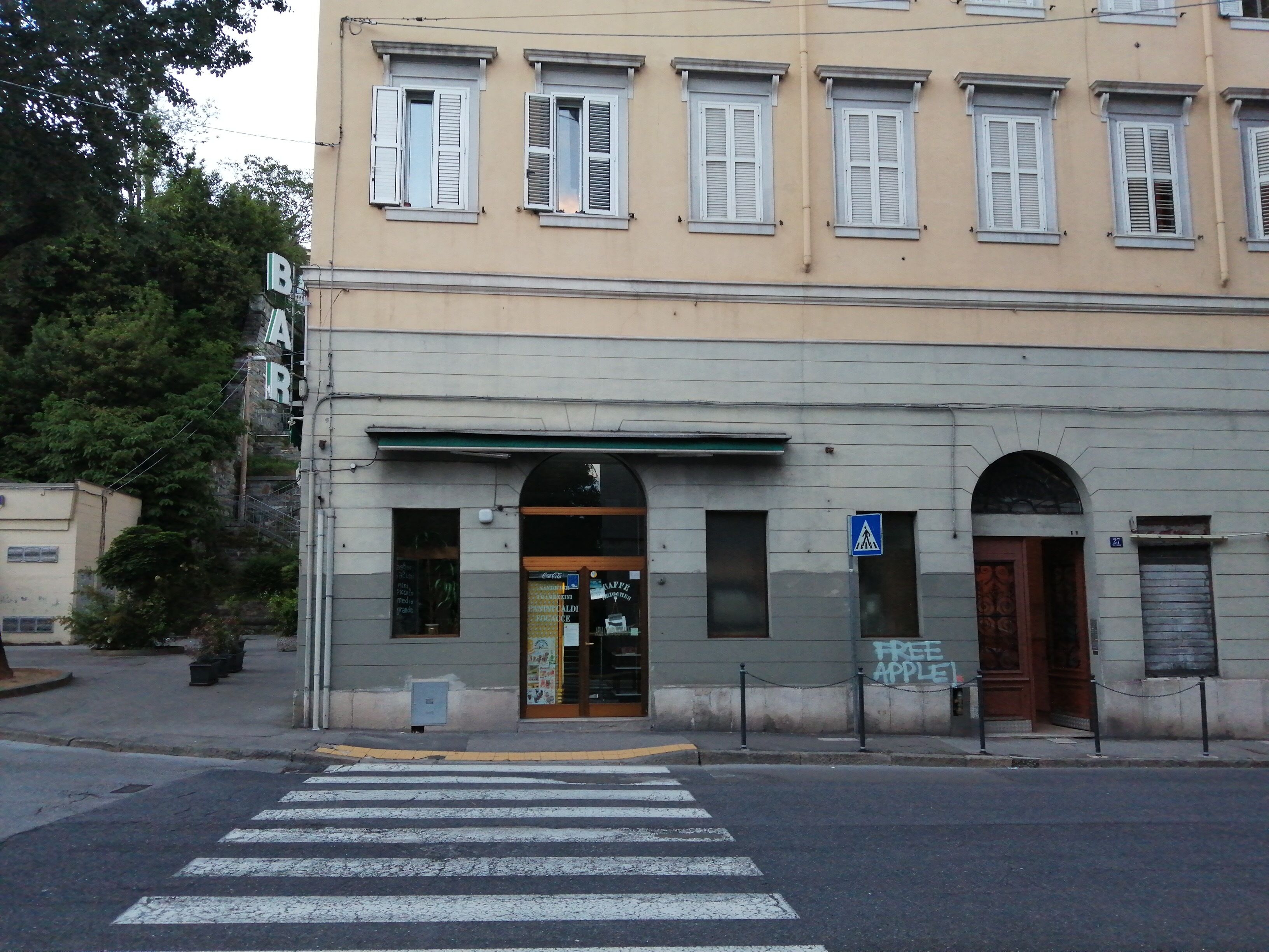 A building with a ground-floor entrance, a pedestrian crossing, and a blue sign indicating a pedestrian crossing.