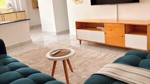 Ein modernes Wohnzimmer mit Türkis-Farbenen Sofas, einem kleinen runden Tisch, einem flachbildfernseher an der Wand und einem Holzkabinett darunter.
