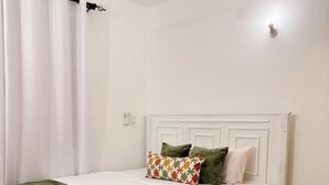 Ein weißes Bett mit grüner Decke, weißen Vorhängen und einem Deckenventilator.