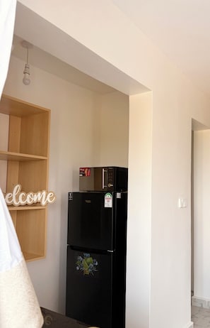 A kitchen with a black refrigerator, a wooden shelf, and a welcome sign. - Modern 1-Bedroom Coastal Apartment in Mtwapa Near the Beach. (Mtwapa)