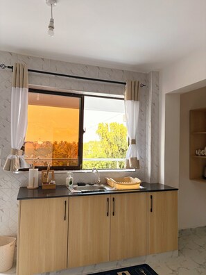 A kitchen with a window, wooden cabinets, a sink, and a countertop. - Modern 1-Bedroom Coastal Apartment in Mtwapa Near the Beach. (Mtwapa)