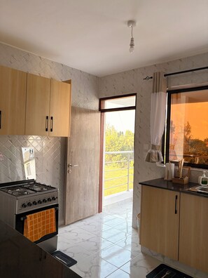 A modern kitchen with wooden cabinets, a gas stove, and a view of greenery outside. - Modern 1-Bedroom Coastal Apartment in Mtwapa Near the Beach. (Mtwapa)
