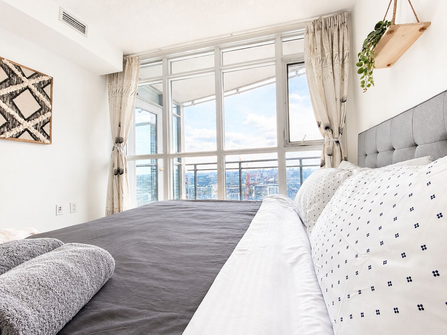 Ein modernes Hotelzimmer mit einem großen Bett, Blick auf die Stadt und einer hängenden Pflanze.