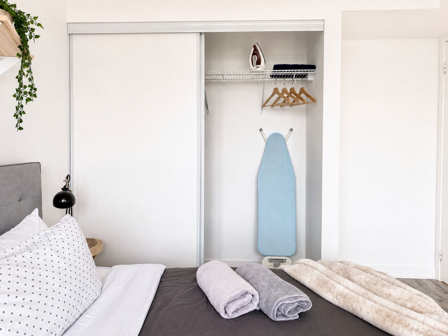 A neatly made bed with a grey and white patterned pillow, a grey blanket, and a rolled-up grey towel.