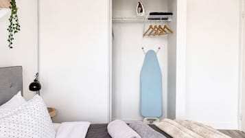 A neatly made bed with a grey and white patterned pillow, a grey blanket, and a rolled-up grey towel.