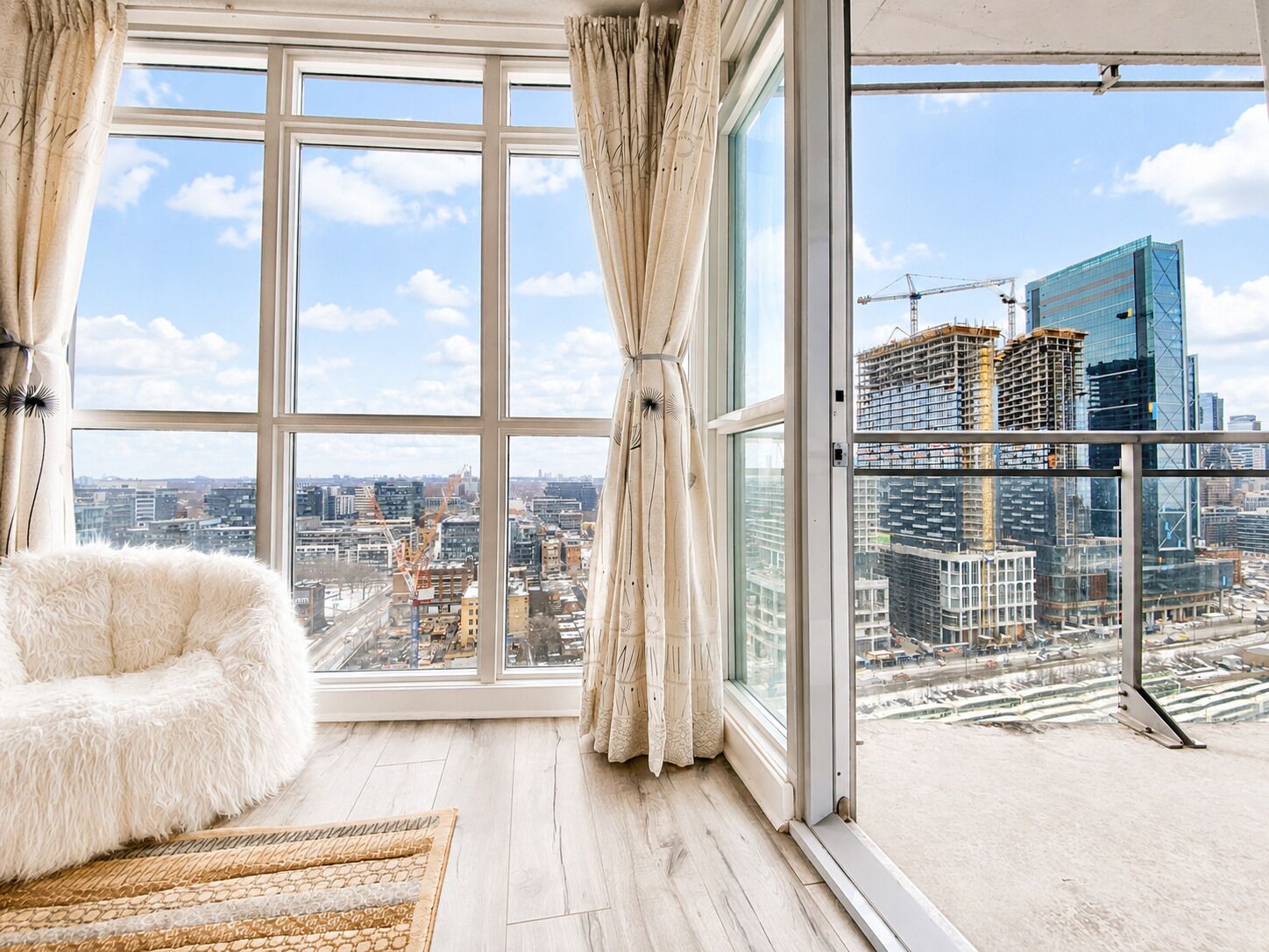 A high-rise room with a large window, a fluffy chair, and a view of the cityscape.