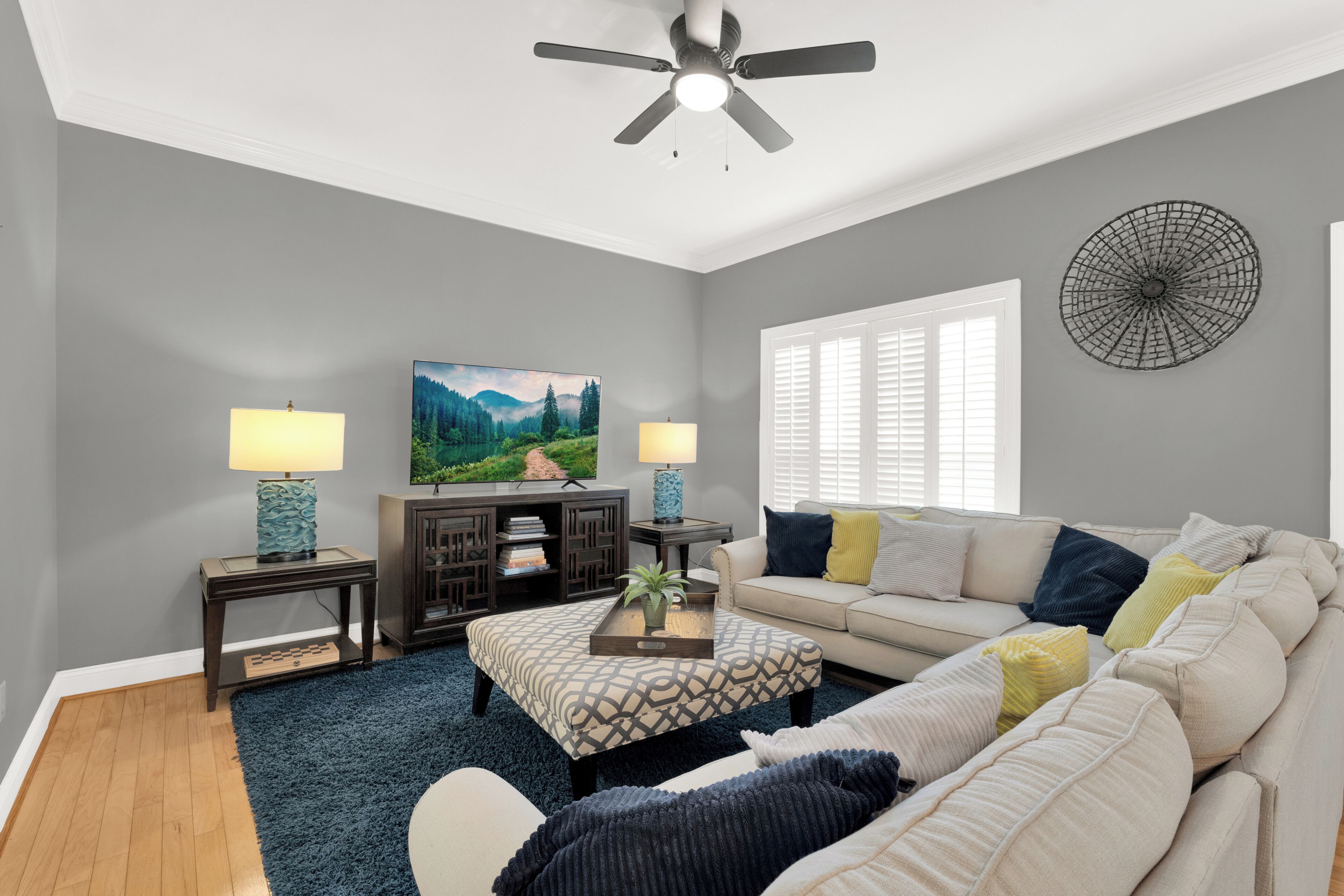 A living room with a ceiling fan, two lamps, a TV, a bookshelf, a sofa, and a window with blinds.