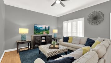 A living room with a ceiling fan, two lamps, a TV, a bookshelf, a sofa, and a window with blinds.