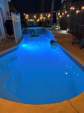 Ein Swimmingpool mit blau beleuchtetem Innenraum, umgeben von einem Holenzaun und Lichterketten.