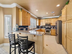 A kitchen with wooden cabinets, a granite countertop, a stainless steel refrigerator, and a built-in oven. - Candy’s Garden Vacation House - Spacious 5-bedroom Las Vegas (Las Vegas)