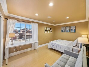 A bedroom with a bed, bedside table, lamp, window with curtains, and artwork on the wall. - Candy’s Garden Vacation House - Spacious 5-bedroom Las Vegas (Las Vegas)