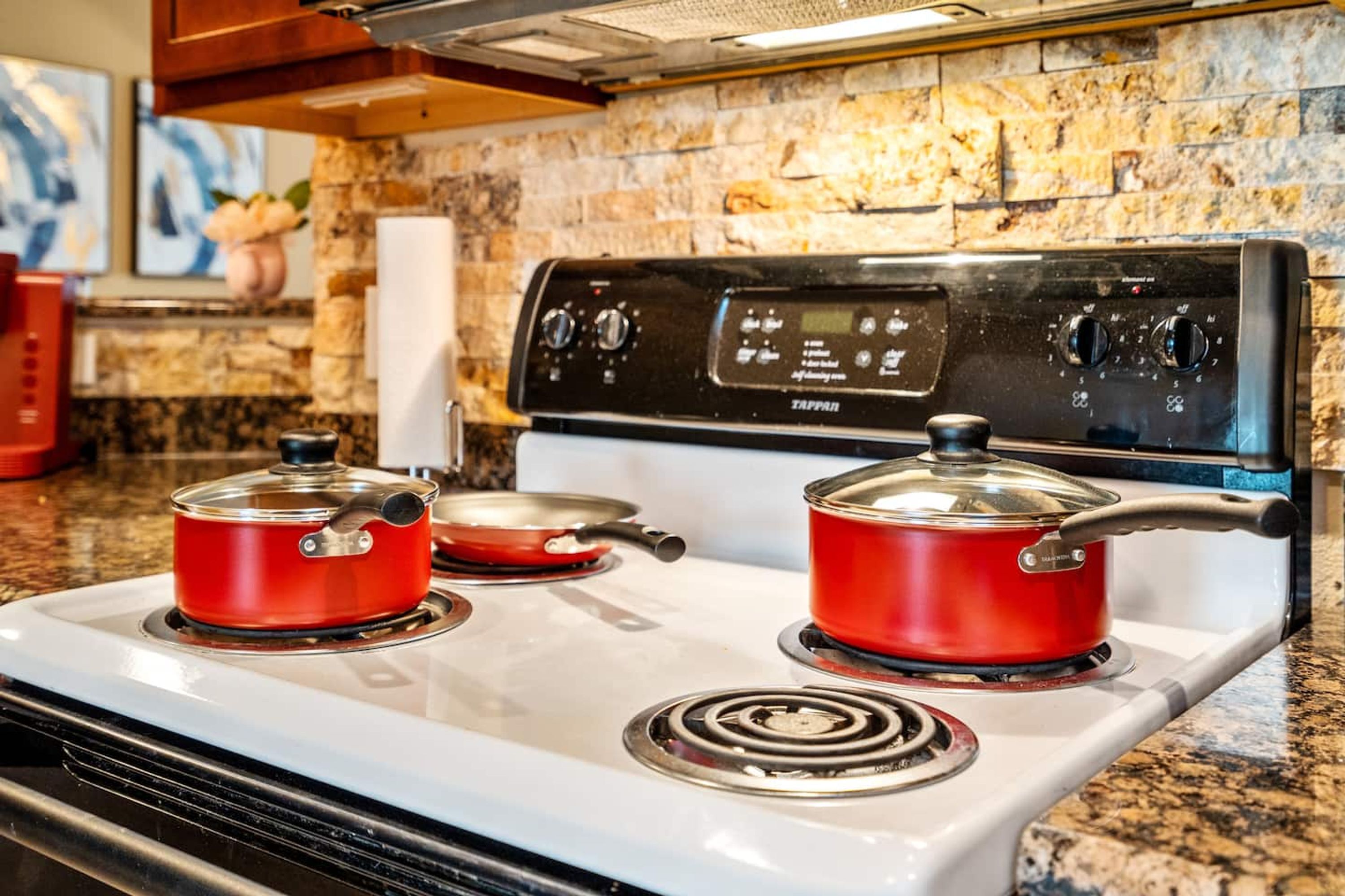 Una cocina con estufa blanca, dos ollas rojas y un salpicadero de piedra.