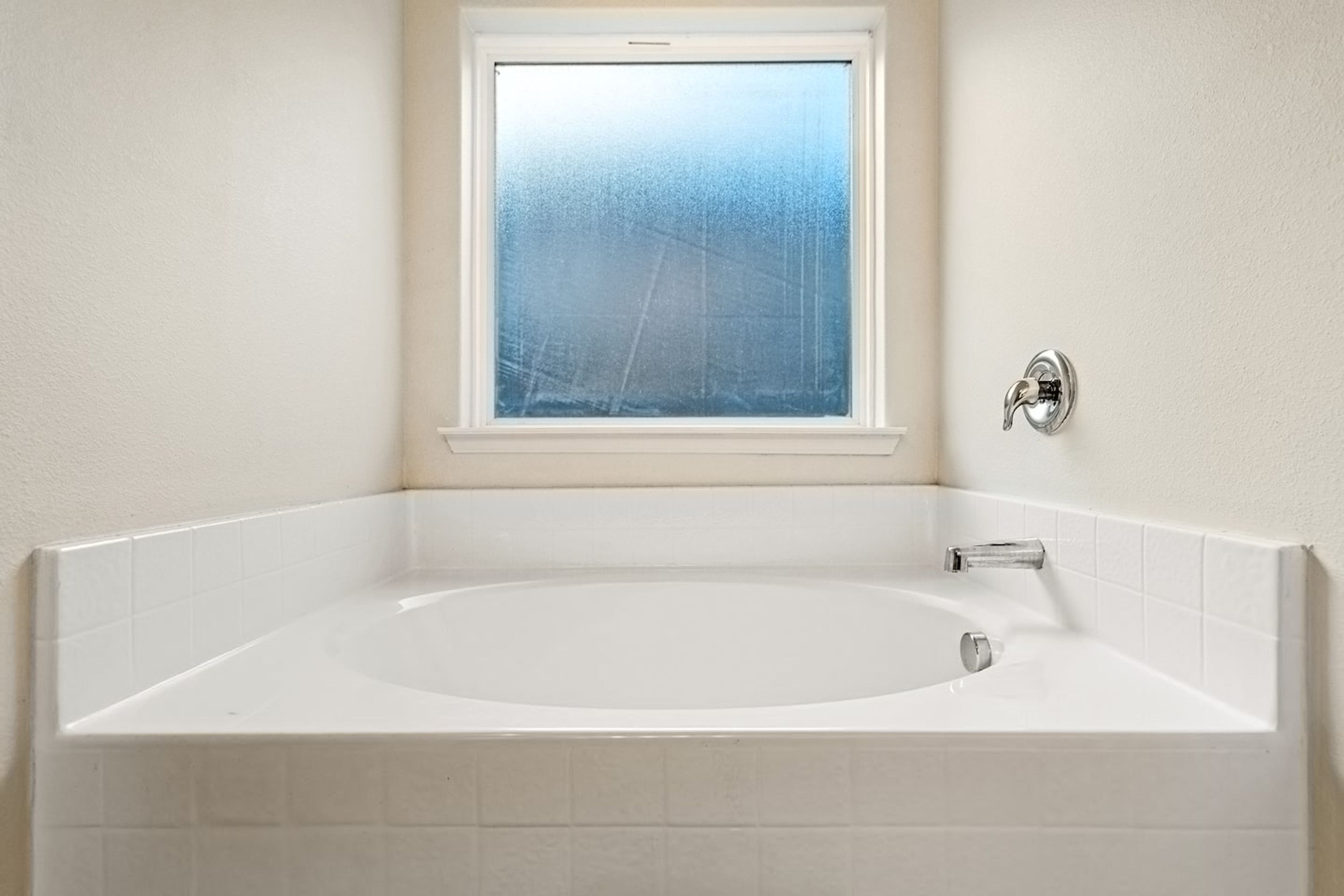 A bathroom with a large bathtub, a window, and a wall-mounted faucet.