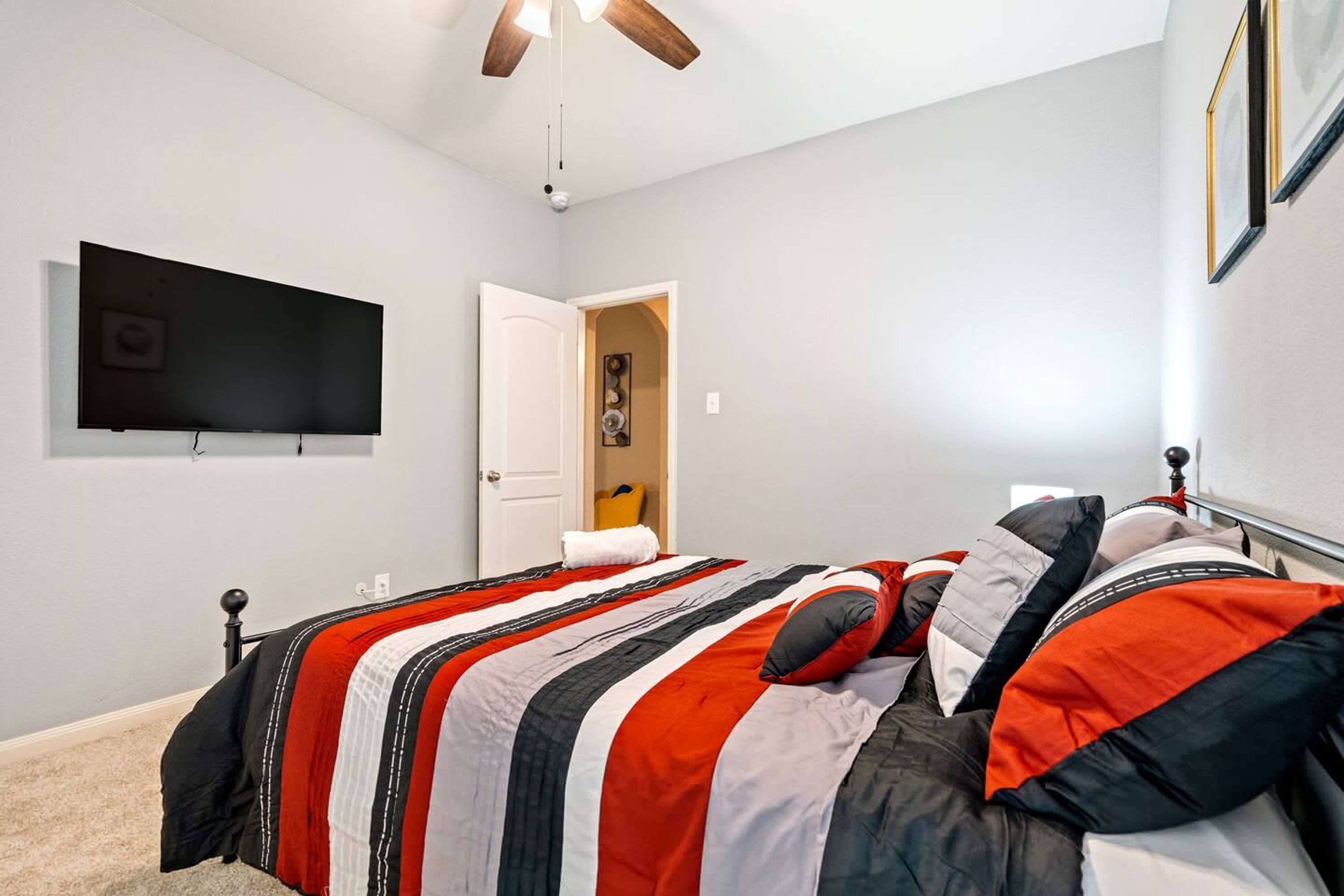 A bedroom with a bed, a television mounted on the wall, and a ceiling fan.