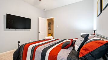 A bedroom with a bed, a television mounted on the wall, and a ceiling fan.