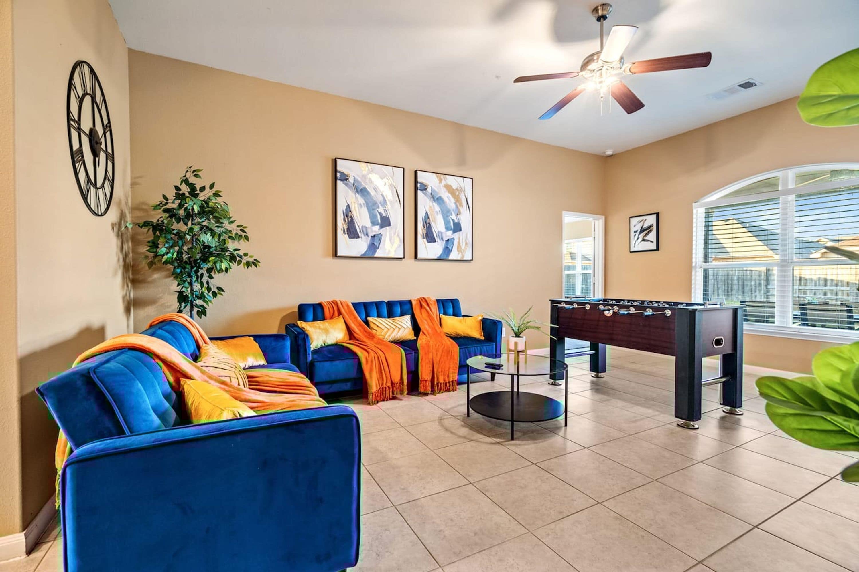 A living room with a blue sofa, a foosball table, and a ceiling fan.