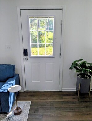 A room with a white door, a blue sofa, a small round table, and a potted plant. - Gorgeous Garden Level Retreat, Close to All! (Charlotte)